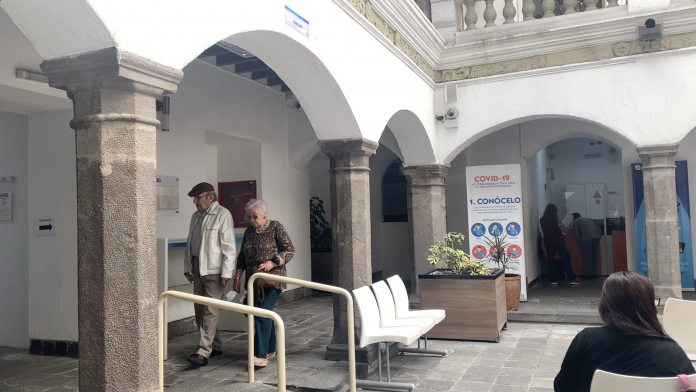 Dos adultos mayores caminan por los pasillos del Municipio de Quito para pagar el impuesto predial.