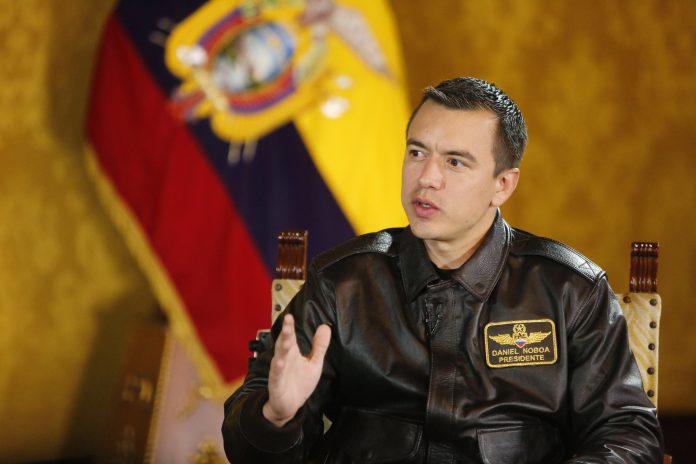 Daniel Noboa, presidente de Ecuador, sentado en una entrevista con la bandera del país en su espalda.